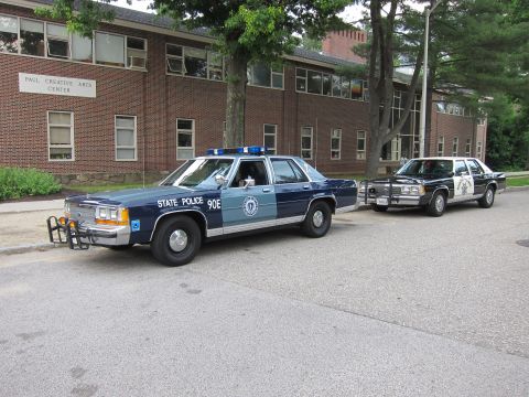 1991 Ford LTD Crown Victoria - two-tone blue Massachusetts State Police sedan marked 90E parked beside a Highway Patrol car at the Paul Creative Arts Center.