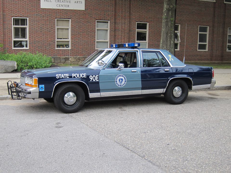 Two-tone blue Massachusetts State Police sedan 90E side view by brick building