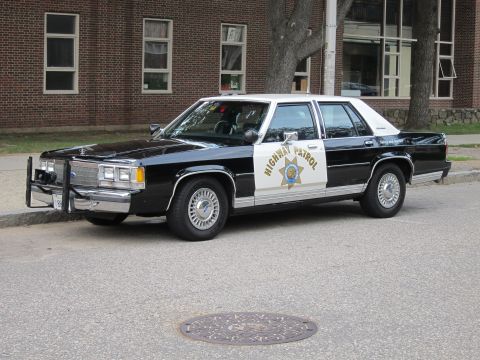 1991 Ford LTD Crown Victoria - Front three-quarter view of a black-and-white Highway Patrol sedan with a gold star decal and push bar, parked on a street.