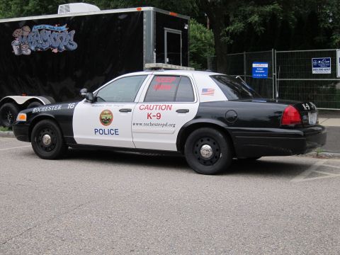 1991 Ford LTD Crown Victoria - black-and-white Rochester Police Ford Crown Victoria marked 'POLICE' and 'CAUTION K-9', parked beside a black enclosed trailer.