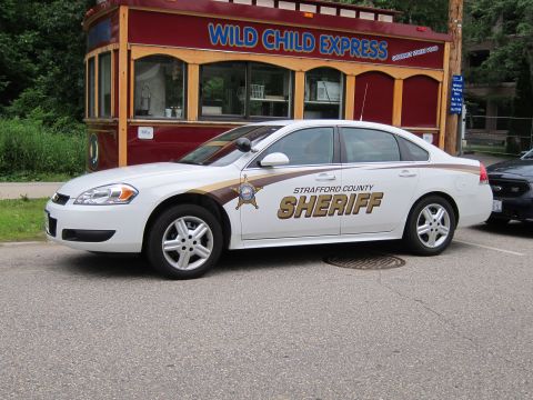 1991 Ford LTD Crown Victoria - white Chevrolet Impala lettered 'STRAFFORD COUNTY SHERIFF' with gold star, parked in front of a red 'Wild Child Express' kiosk.