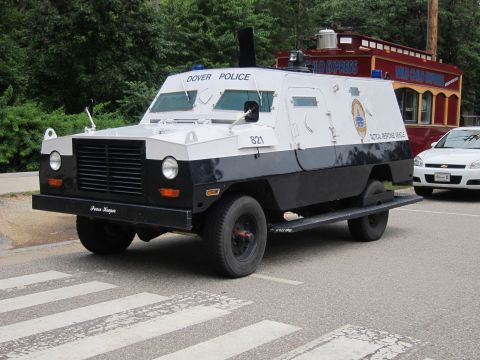 1991 Ford LTD Crown Victoria - boxy white and dark blue Dover Police armored tactical response truck marked '821' sits at a crosswalk near a red trolley.