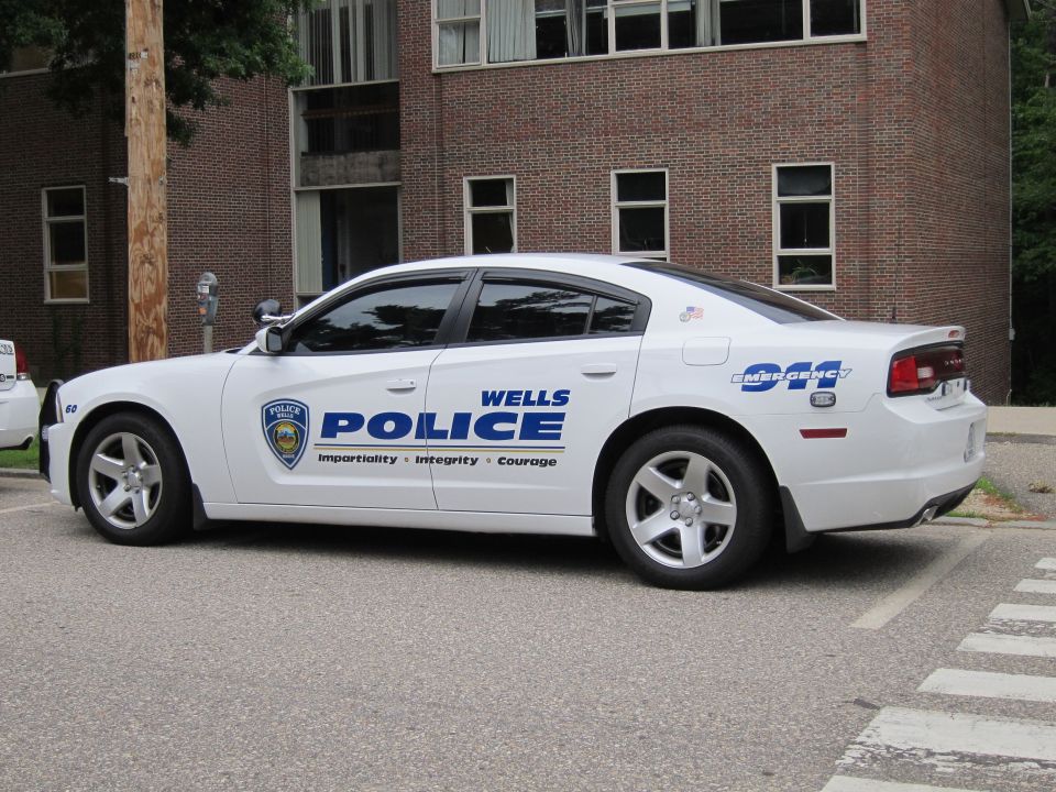 White Wells Police Dodge Charger sedan parked beside a brick building