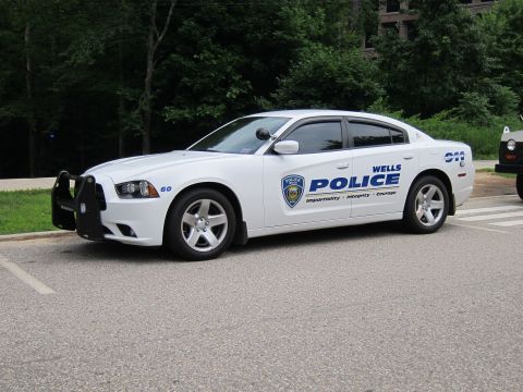 1991 Ford LTD Crown Victoria - white Wells Police Dodge Charger unit 60 with push bar parked along a roadside with a green wooded backdrop.