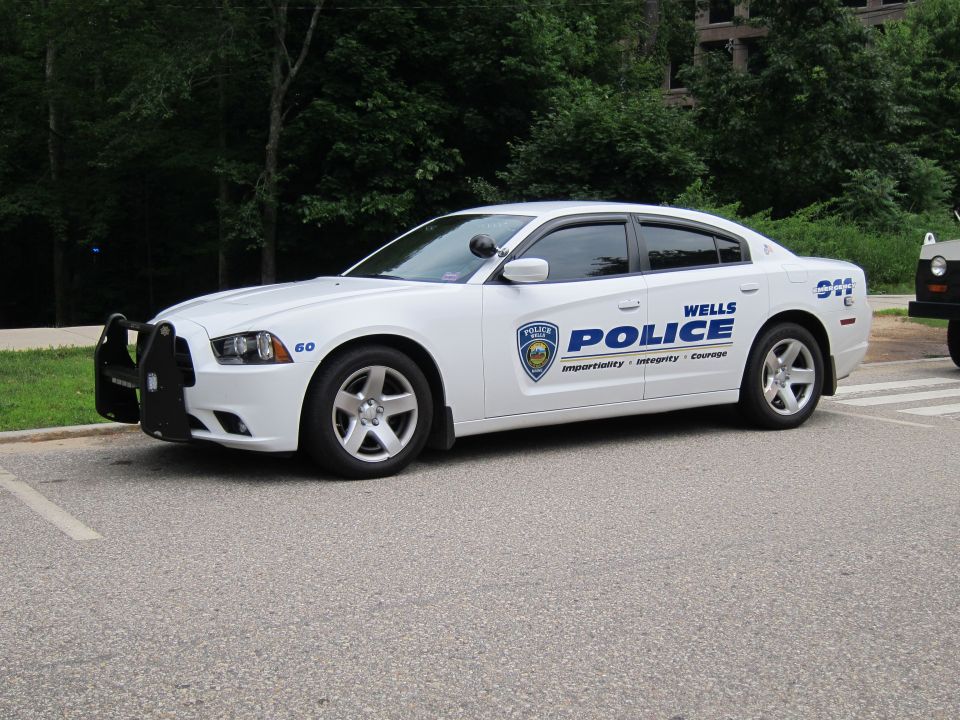 White Wells Police Dodge Charger sedan parked along a roadside near trees