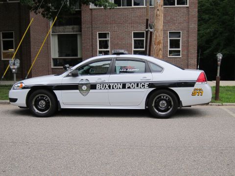 1991 Ford LTD Crown Victoria - black and white Chevrolet Impala marked 'Buxton Police' parked at a curb in front of a brick building.