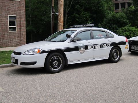 1991 Ford LTD Crown Victoria - white and black Chevrolet Impala marked 'Buxton Police' parked on a road by a brick building.
