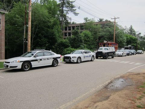 1991 Ford LTD Crown Victoria - row of police vehicles including Buxton Police cruisers and a dark armored truck lined up along a tree-lined road.