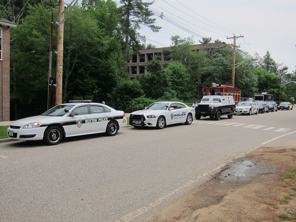 Line of police cruisers and an armored truck parked along a wooded road