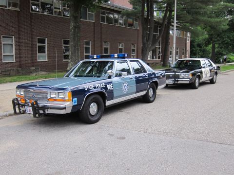 1991 Ford LTD Crown Victoria - Two two-tone blue Ford LTD Crown Victoria 'State Police 90E' cruisers parked in front of a brick building.