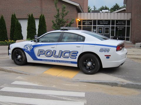 1991 Ford LTD Crown Victoria - white and blue Dodge Charger marked 'Police University of New Hampshire' parked outside an arts center.