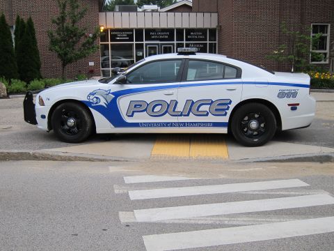 1991 Ford LTD Crown Victoria - Side view of a white and blue Dodge Charger marked 'Police University of New Hampshire' stopped at a crosswalk.