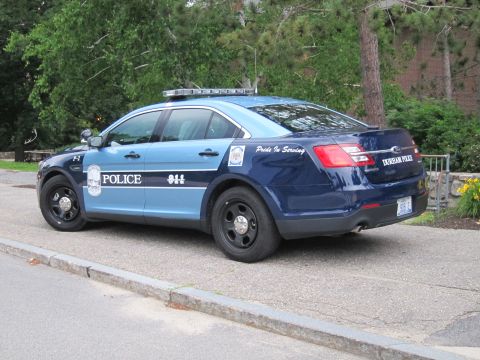 1991 Ford LTD Crown Victoria - two-tone blue Ford police sedan marked Police with light bar, parked at a curb by a brick building and trees.
