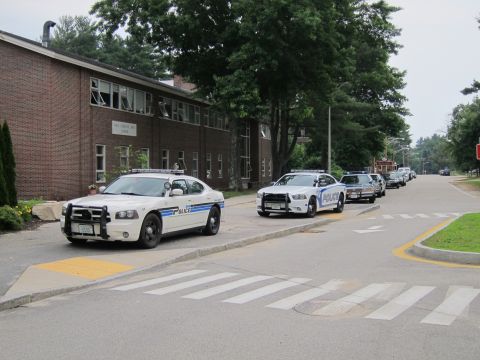 1991 Ford LTD Crown Victoria - line of police cruisers and other vehicles staged along a street beside a brick building at an intersection.