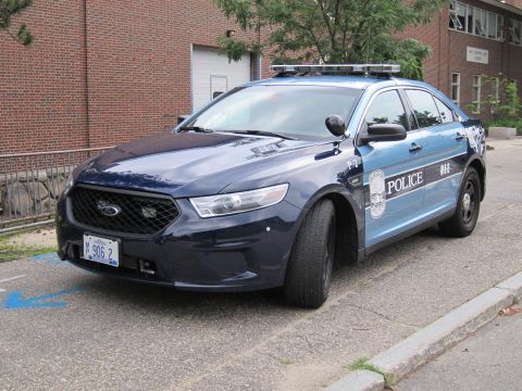 1991 Ford LTD Crown Victoria - dark blue Ford police sedan with lightbar and plate MP 906 2 parked along a curb by a brick building.