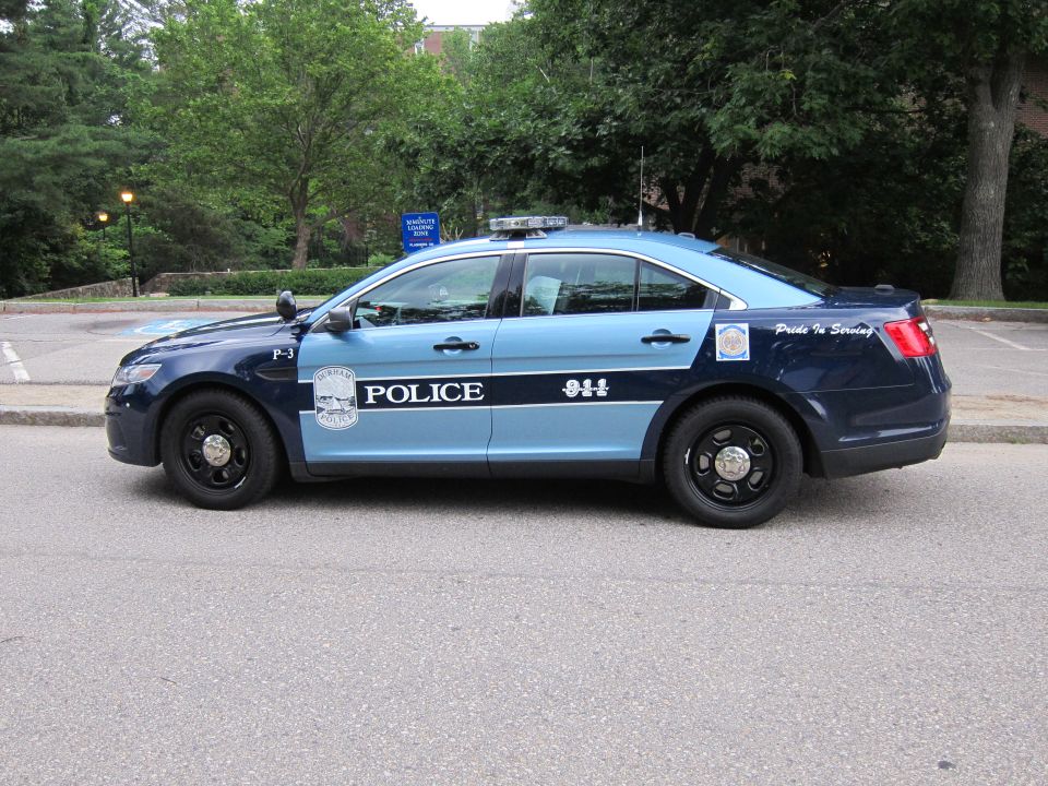 Two-tone blue Ford police sedan, driver-side profile by a road