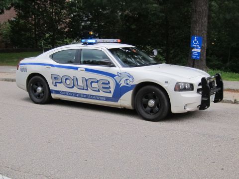 1991 Ford LTD Crown Victoria - white Dodge Charger marked Police University of New Hampshire with a blue wildcat logo and push bar, parked on a street.