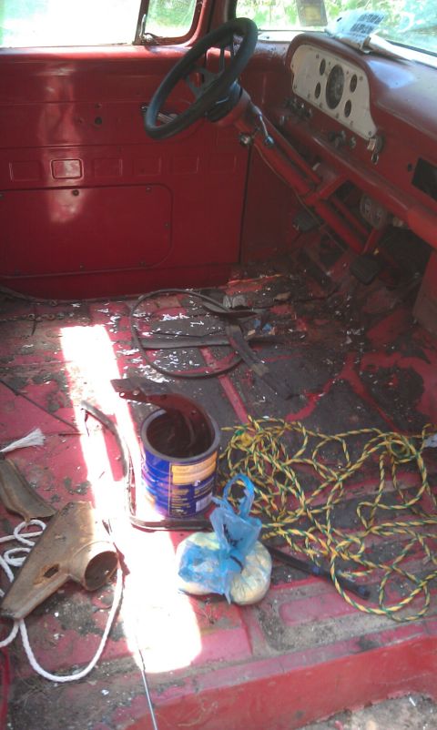 1957 Ford F-100 - Interior view of a 1957 Ford F-100 cab, showing the dashboard, steering wheel, and a messy floor.