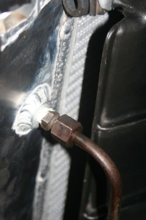 1976 Ford Ranchero - Close-up of a radiator hose fitting, showing metal tubing and sealant against a textured surface.