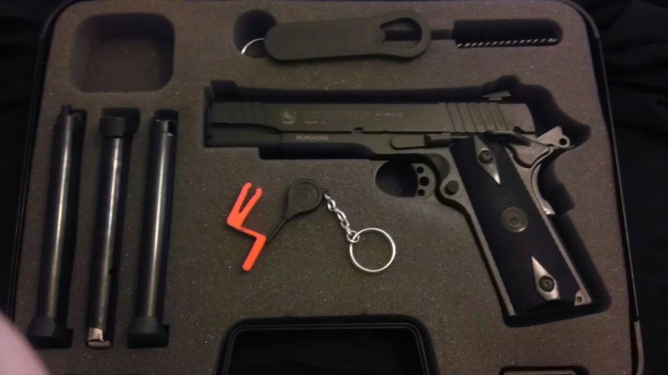 Black pistol with three magazines, cleaning brush, and orange safety device in a foam-lined case