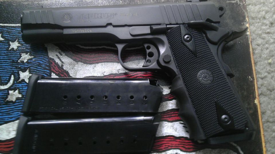 Black Taurus pistol with two magazines on a surface with an American flag design