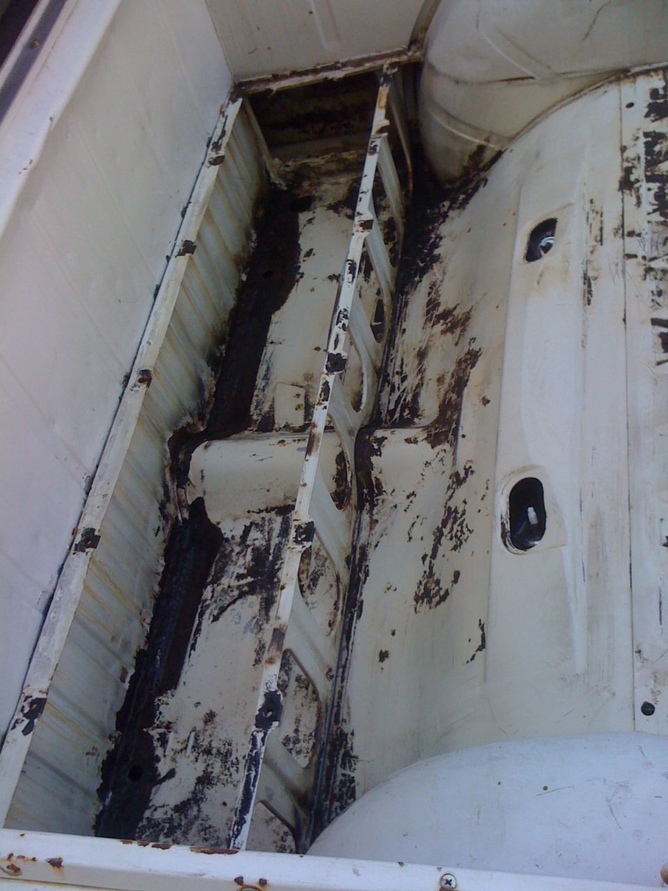 Inside of a truck bed, showing rust and damage to the metal structure