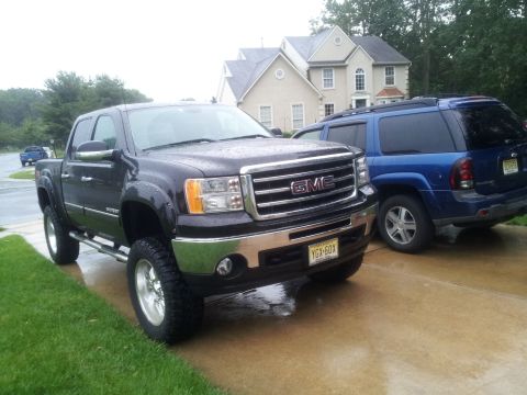 1978 Chevrolet C/K Pickup - A dark GMC Sierra pickup truck is parked on a wet driveway, with a blue SUV behind it.