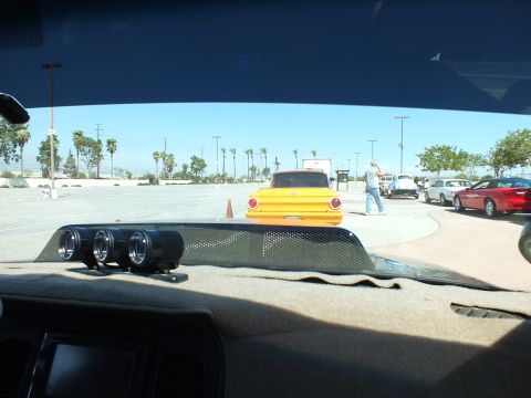 2003 Ford Crown Victoria - yellow vintage pickup truck sits across a sunny parking lot, viewed through a windshield over a dashboard with three round gauges.