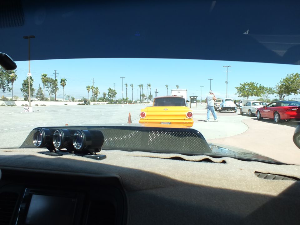 Yellow vintage pickup truck seen through a windshield across a parking lot
