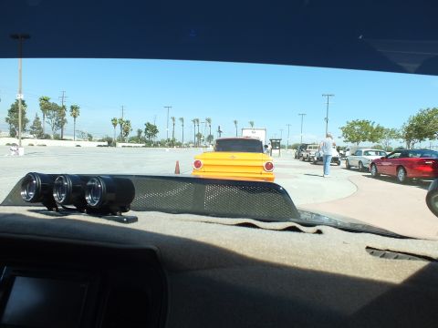 2003 Ford Crown Victoria - yellow vintage pickup truck across a parking lot, seen through a windshield with three round dashboard gauges in the foreground.