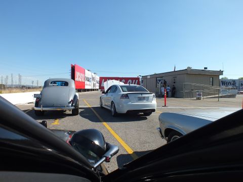 2003 Ford Crown Victoria - vintage black hot rod and a silver sedan parked at a drag strip facility with Lucas Oil and Wix banners in the background.