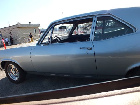 2003 Ford Crown Victoria - silver two-door muscle car shown in profile at a drag strip, with a number written on the rear window and pit buildings behind.