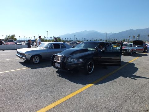 2003 Ford Crown Victoria - black full-size sedan with a chrome grille guard parked next to a silver classic car under a clear sky with mountains behind.