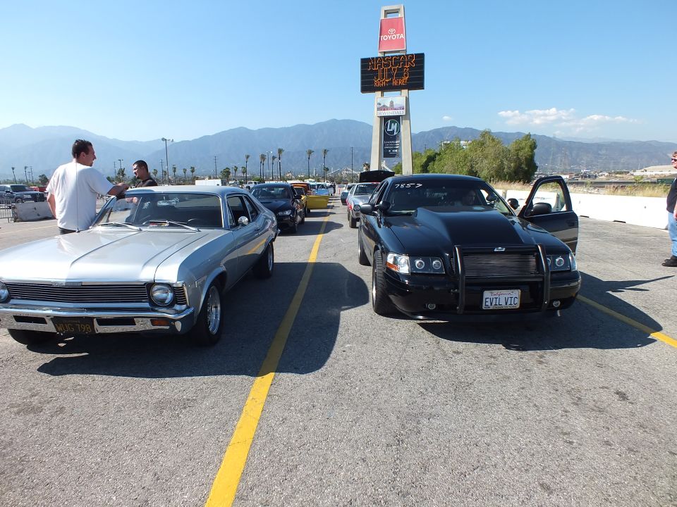 Silver classic muscle car and black sedan parked nose-to-nose in a lot