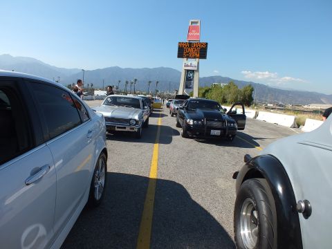 2003 Ford Crown Victoria - Looking down a line of cars staged at a drag strip, with a white sedan and a black hot rod fender framing the view under an NHRA sign.