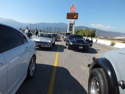 2003 Ford Crown Victoria - Vehicles wait in the staging lanes beneath the Irwindale Dragstrip tower sign, with a silver muscle car and black sedan flanking a center l…