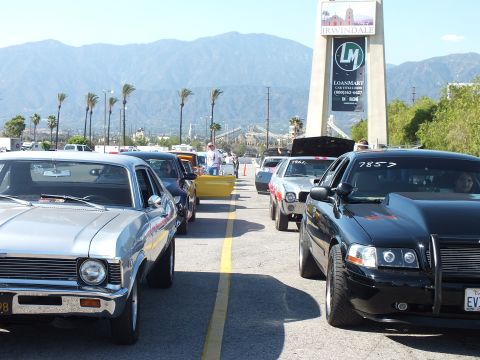2003 Ford Crown Victoria - silver Chevrolet Nova and a black sedan marked 7857 wait in the staging lanes beneath the Irwindale LoanMart tower sign with palms and moun…