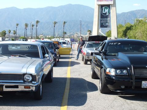 2003 Ford Crown Victoria - man stands in the staging lane between a silver Chevrolet Nova and a black sedan numbered 7857 under the Irwindale LoanMart tower sign.