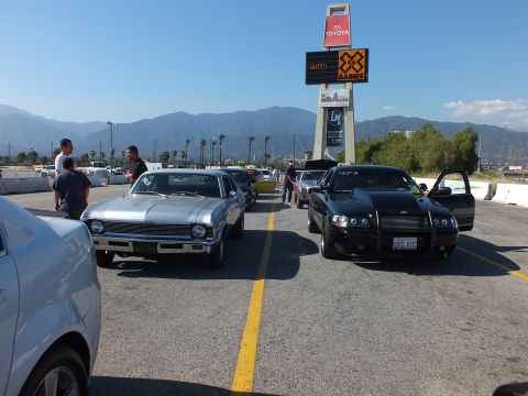 2003 Ford Crown Victoria - silver Chevrolet Nova faces forward beside a black sedan in the staging lanes under an Irwindale tower sign advertising X Games, with onloo…