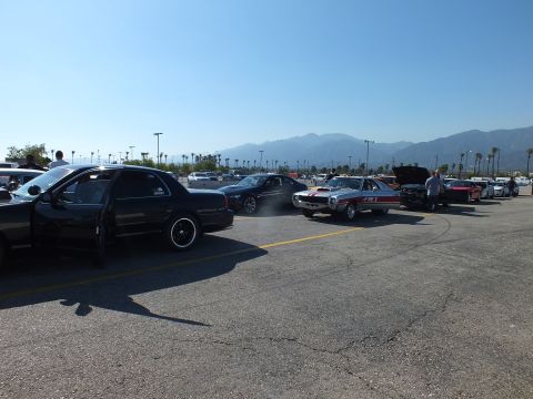 2003 Ford Crown Victoria - Cars stage on the drag-strip apron including a black sedan and a red-and-white striped muscle car, with mountains rising in the haze beyond.