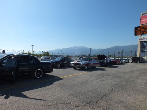2003 Ford Crown Victoria - wide view of the drag-strip staging area shows a black sedan, a striped muscle car, and hood-up vehicles lined toward a distant Toyota towe…