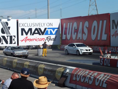 2003 Ford Crown Victoria - silver muscle car and a white Pontiac G8 sedan stage at the start line before a starter, framed by MavTV and Lucas Oil banners.
