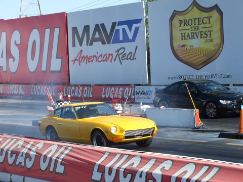 2003 Ford Crown Victoria - yellow Datsun 240Z stages at the start line beside the burnout box, with MavTV and Protect the Harvest banners on the wall behind.