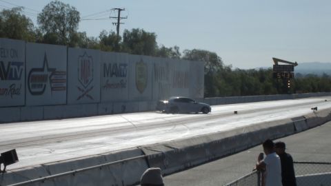 2003 Ford Crown Victoria - silver coupe accelerates down the drag strip beside MavTV and other sponsor banners, with the timing scoreboard at the far right.