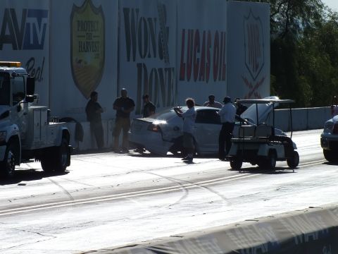 2003 Ford Crown Victoria - Crew members and a tow truck surround a wrecked white car pushed against the strip wall beneath Won & Done and Lucas Oil banners.