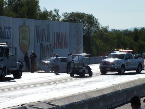 2003 Ford Crown Victoria - tow truck, golf cart, and safety pickup converge on a crashed car at the drag-strip wall while crew works under sponsor banners.