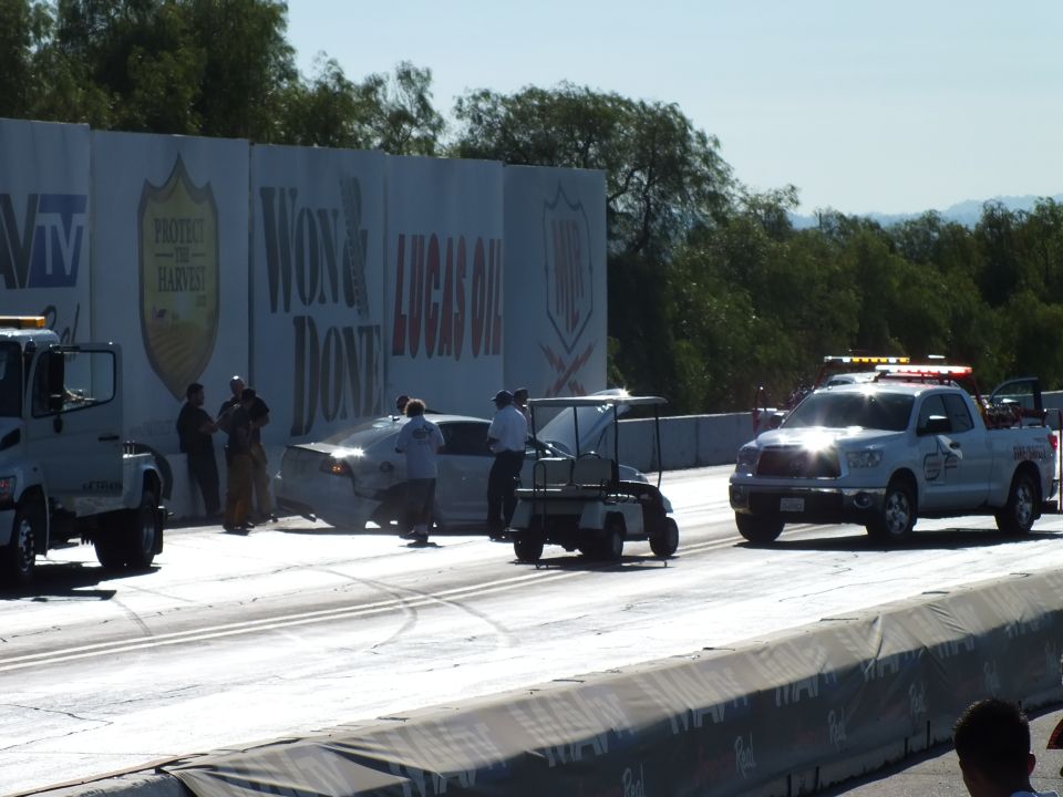 Tow truck, golf cart, and safety pickup at a crash scene along the drag-strip wall