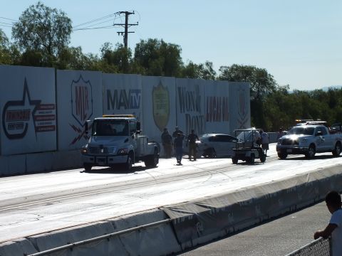 2003 Ford Crown Victoria - Recovery vehicles and crew line up along the strip wall during a crash cleanup, with MavTV, Won & Done, and Lucas Oil banners overhead.