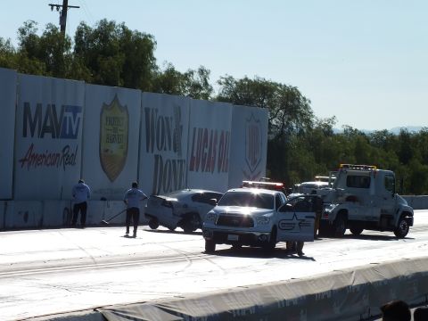 2003 Ford Crown Victoria - tow truck hooks up a wrecked car while crew members sweep the track surface beside MavTV, Won & Done, and Lucas Oil wall banners.