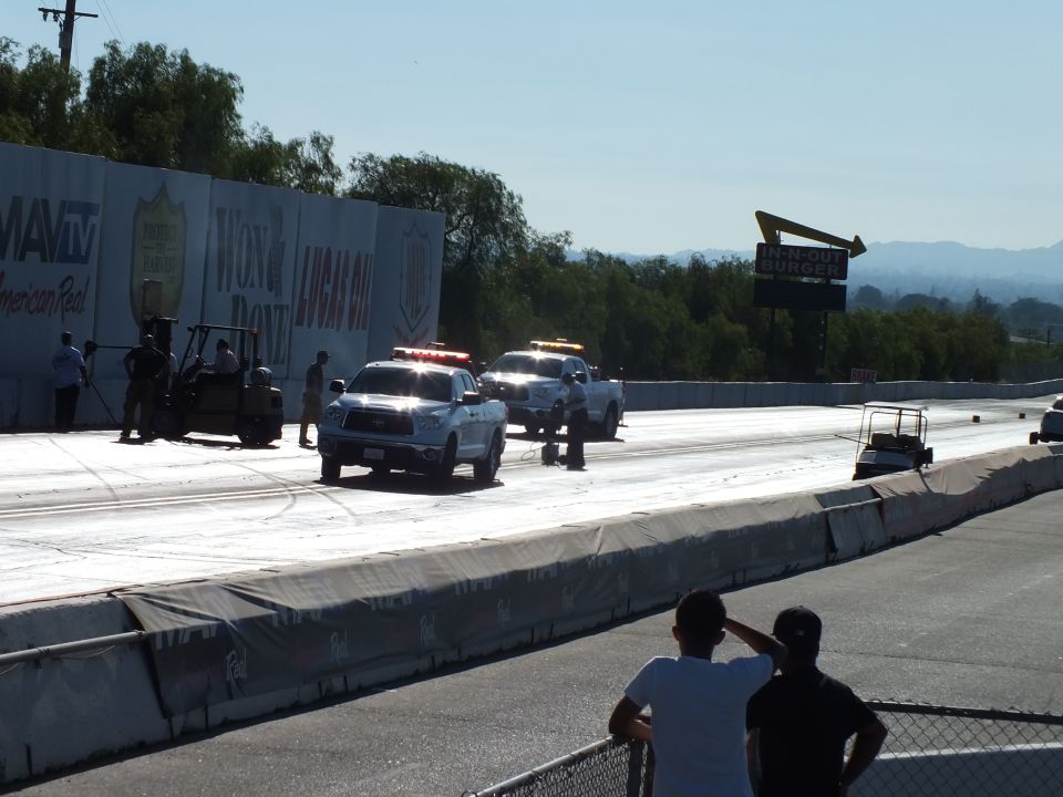 White trucks parked on drag strip beside sponsor banner wall